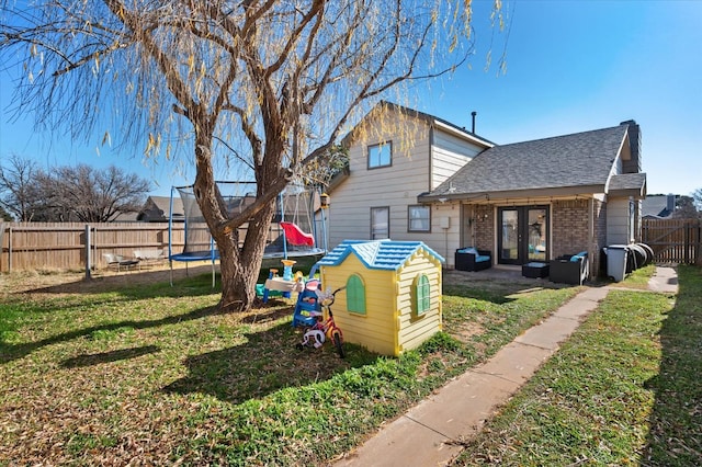 rear view of house with french doors, a yard, and a trampoline