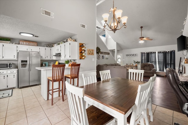 tiled dining space with high vaulted ceiling, ceiling fan with notable chandelier, and a textured ceiling