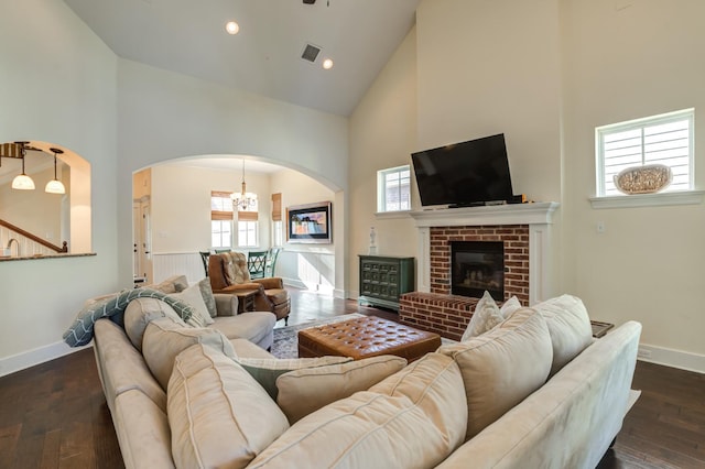 living room featuring an inviting chandelier, a fireplace, dark wood-type flooring, and high vaulted ceiling