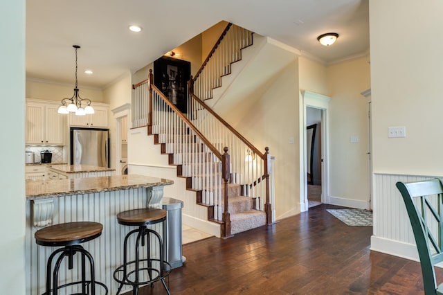 interior space with dark wood-type flooring, a kitchen bar, crown molding, stainless steel refrigerator, and light stone countertops