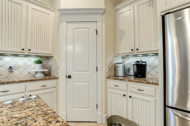 kitchen featuring cream cabinetry, stone countertops, stainless steel fridge, and backsplash