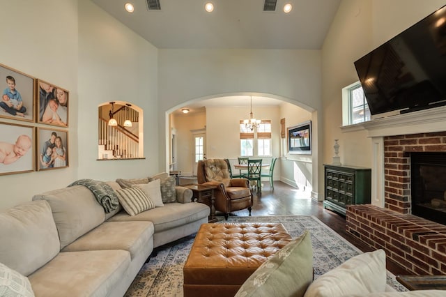 living room with high vaulted ceiling, a fireplace, a chandelier, and hardwood / wood-style floors