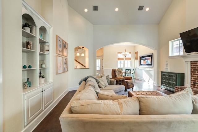 living room featuring a high ceiling, a brick fireplace, a notable chandelier, and dark hardwood / wood-style flooring