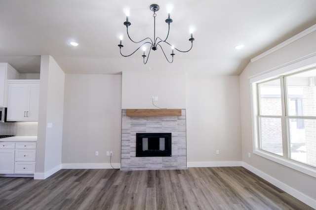 unfurnished living room featuring a chandelier, a tiled fireplace, wood finished floors, and baseboards