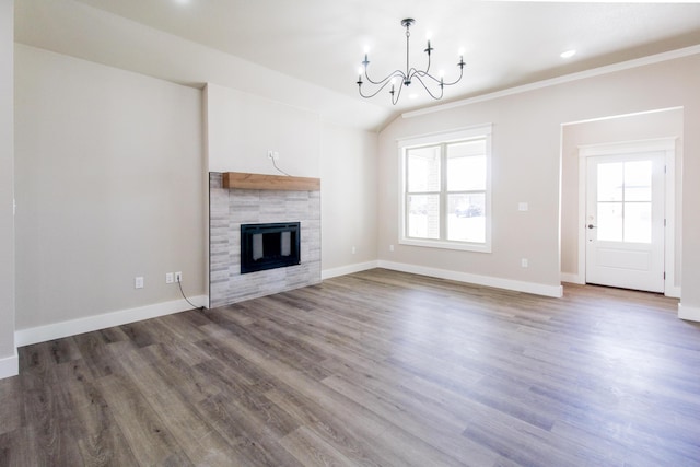 unfurnished living room with a tile fireplace, a notable chandelier, wood finished floors, and baseboards