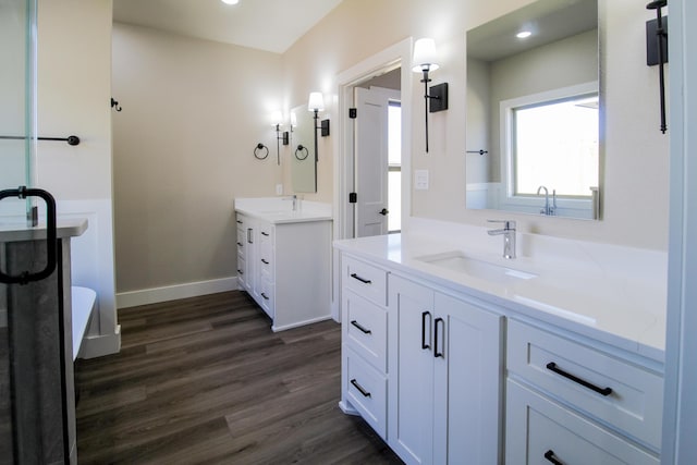 bathroom featuring two vanities, wood finished floors, recessed lighting, and a sink