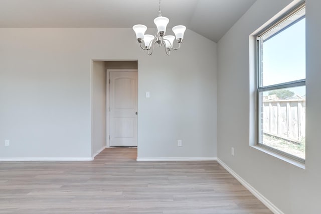 empty room with vaulted ceiling, an inviting chandelier, and light hardwood / wood-style flooring