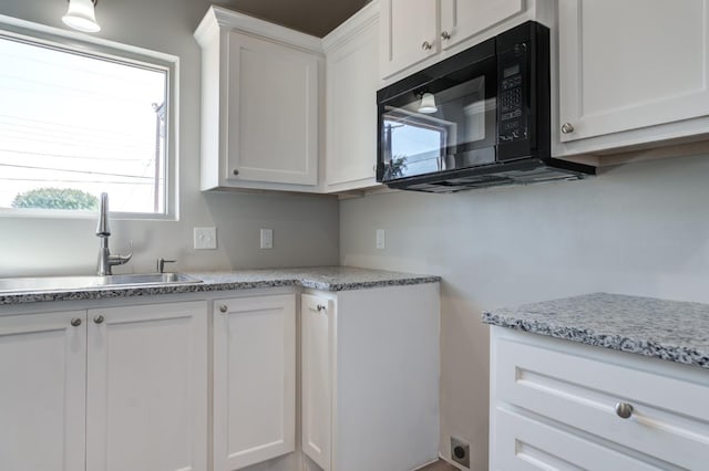 kitchen with white cabinetry, sink, and light stone counters