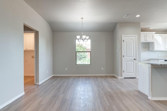 unfurnished dining area with an inviting chandelier and light hardwood / wood-style flooring