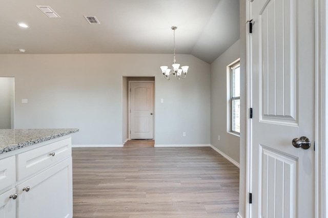 kitchen with pendant lighting, lofted ceiling, white cabinetry, light stone counters, and light hardwood / wood-style floors