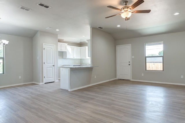 unfurnished living room featuring lofted ceiling, ceiling fan with notable chandelier, and light hardwood / wood-style floors