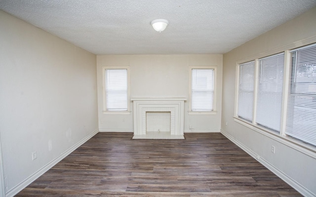 unfurnished living room featuring dark wood-type flooring, plenty of natural light, a brick fireplace, and a textured ceiling