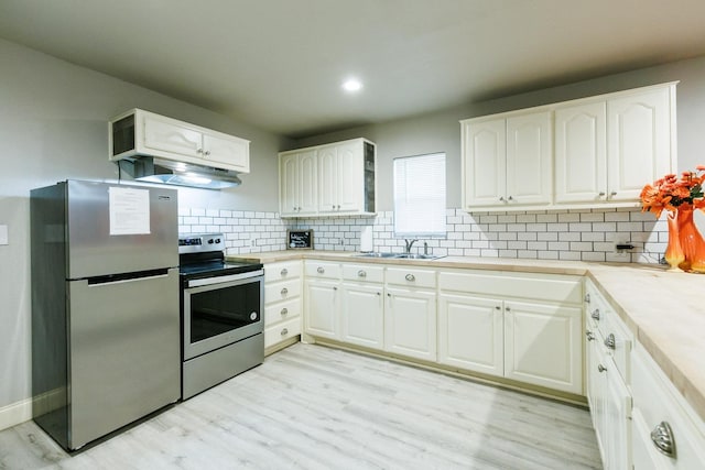 kitchen with appliances with stainless steel finishes, tasteful backsplash, sink, white cabinets, and light hardwood / wood-style flooring