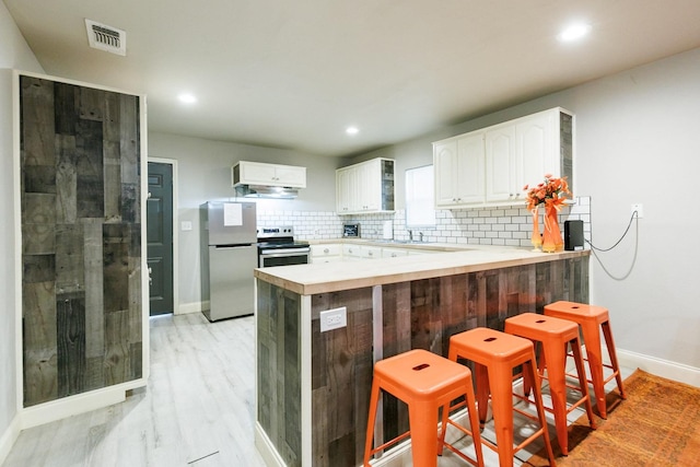 kitchen featuring white cabinetry, appliances with stainless steel finishes, a kitchen breakfast bar, kitchen peninsula, and backsplash