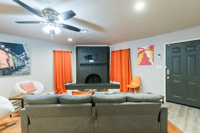 living room featuring a brick fireplace, ceiling fan, and light wood-type flooring