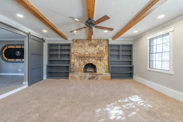 unfurnished living room featuring beam ceiling, ornamental molding, a barn door, and a textured ceiling