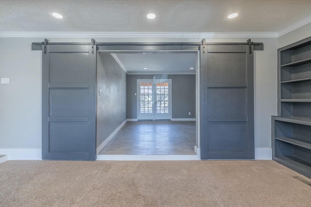 unfurnished living room with crown molding, carpet, a textured ceiling, built in shelves, and a barn door