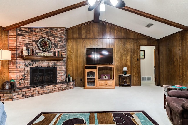 carpeted living room featuring ceiling fan, a fireplace, wooden walls, and vaulted ceiling with beams