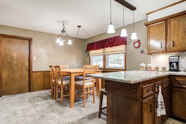 kitchen with wooden walls, light carpet, a textured ceiling, and decorative light fixtures