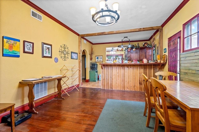 dining room featuring ornamental molding, indoor bar, dark wood-type flooring, and a chandelier