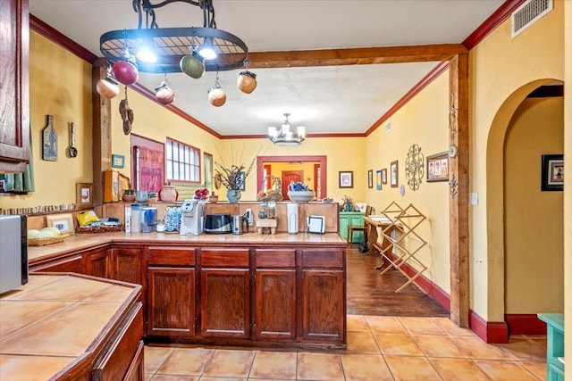 kitchen featuring crown molding, tile counters, a chandelier, and kitchen peninsula