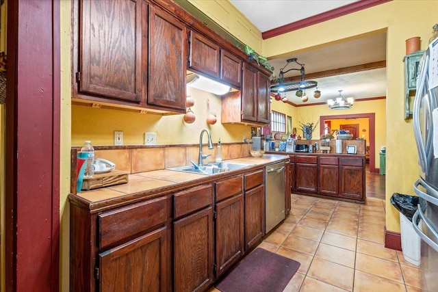 kitchen featuring sink, light tile patterned floors, appliances with stainless steel finishes, tile counters, and decorative light fixtures