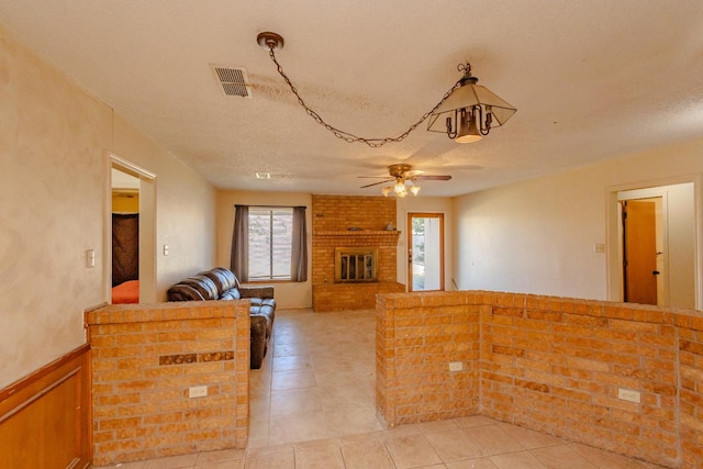 living room with ceiling fan, light tile patterned floors, a brick fireplace, and a textured ceiling