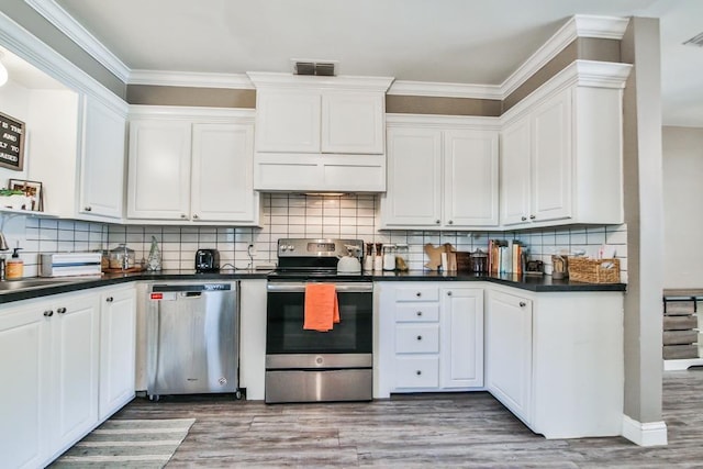 kitchen with appliances with stainless steel finishes, white cabinetry, decorative backsplash, ornamental molding, and light hardwood / wood-style flooring