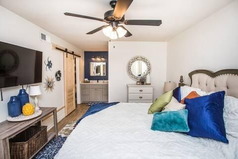 bedroom featuring hardwood / wood-style flooring, ensuite bath, a barn door, and ceiling fan