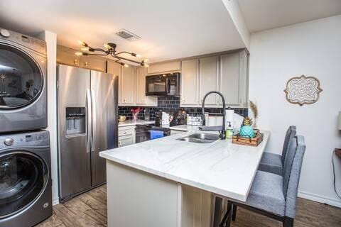 kitchen with stacked washer / drying machine, sink, stainless steel fridge with ice dispenser, kitchen peninsula, and backsplash