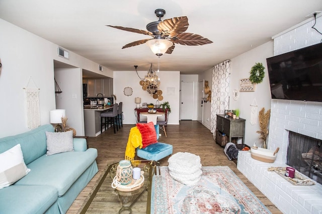 living room with hardwood / wood-style floors, ceiling fan with notable chandelier, and a brick fireplace