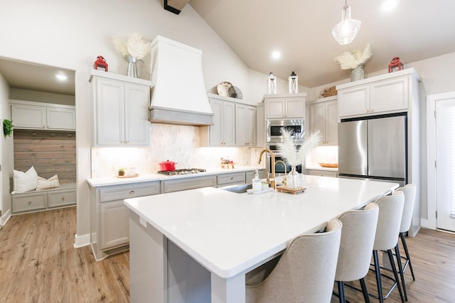 kitchen featuring sink, custom exhaust hood, an island with sink, pendant lighting, and stainless steel appliances