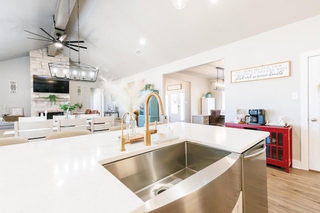 kitchen featuring a fireplace, decorative light fixtures, lofted ceiling, sink, and light wood-type flooring