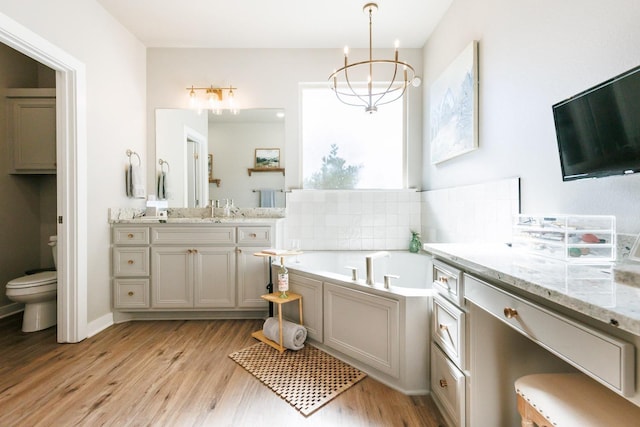 bathroom with toilet, vanity, a bathtub, a notable chandelier, and hardwood / wood-style floors