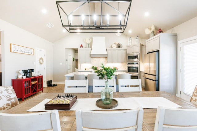 kitchen featuring premium range hood, appliances with stainless steel finishes, white cabinets, hanging light fixtures, and light hardwood / wood-style flooring