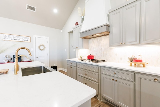 kitchen featuring lofted ceiling, sink, gray cabinets, decorative backsplash, and custom exhaust hood