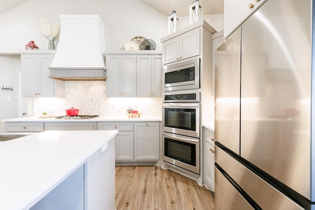 kitchen with premium range hood, stainless steel appliances, tasteful backsplash, white cabinets, and light wood-type flooring