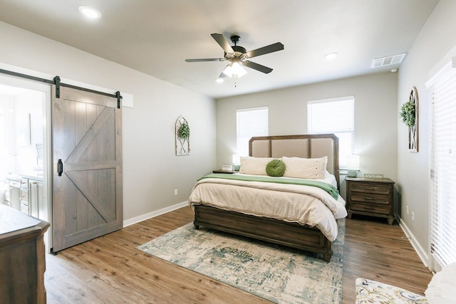 bedroom featuring a barn door, hardwood / wood-style floors, and ceiling fan