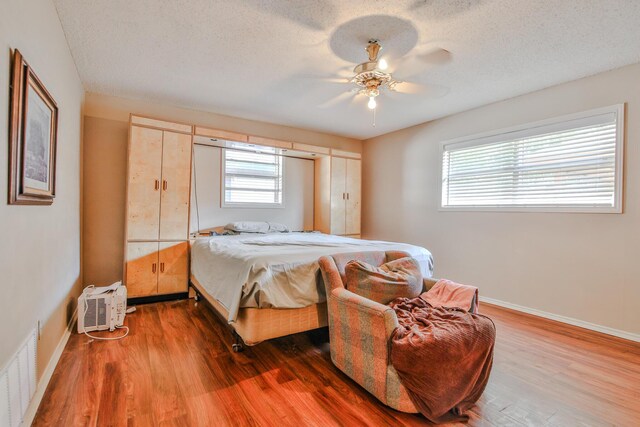 bedroom featuring ceiling fan, a wall mounted air conditioner, hardwood / wood-style floors, and a textured ceiling