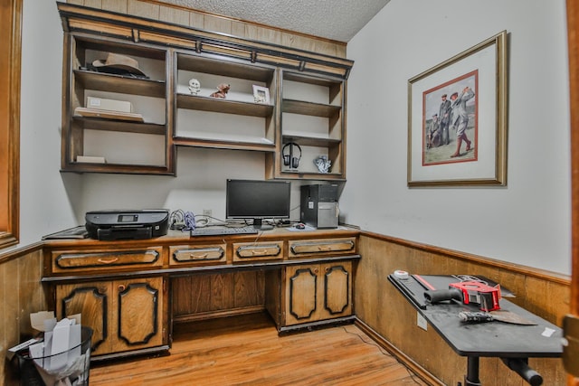 office with built in desk, a textured ceiling, light wood-type flooring, and wood walls