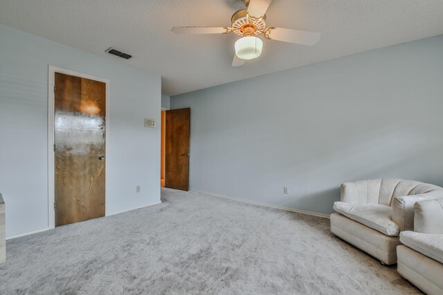 living area featuring ceiling fan, light carpet, and a textured ceiling