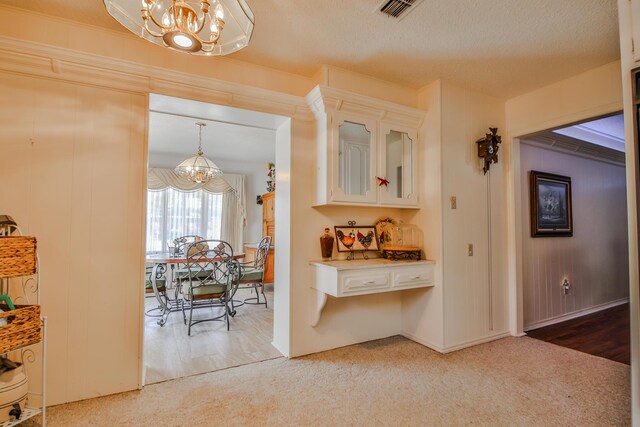 interior space with pendant lighting, carpet flooring, a notable chandelier, a textured ceiling, and white cabinets