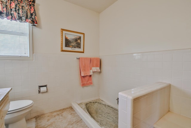 bathroom with tile walls, vanity, a tub, and toilet