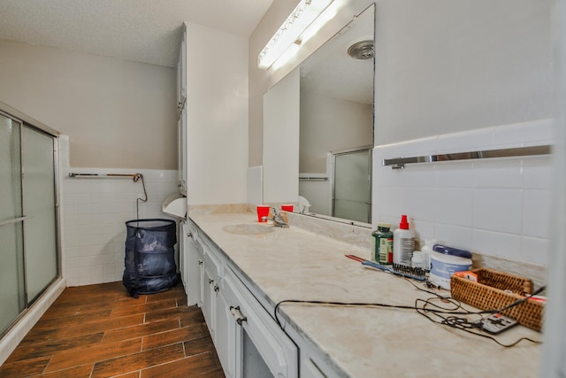 bathroom featuring wood-type flooring, tile walls, vanity, walk in shower, and a textured ceiling