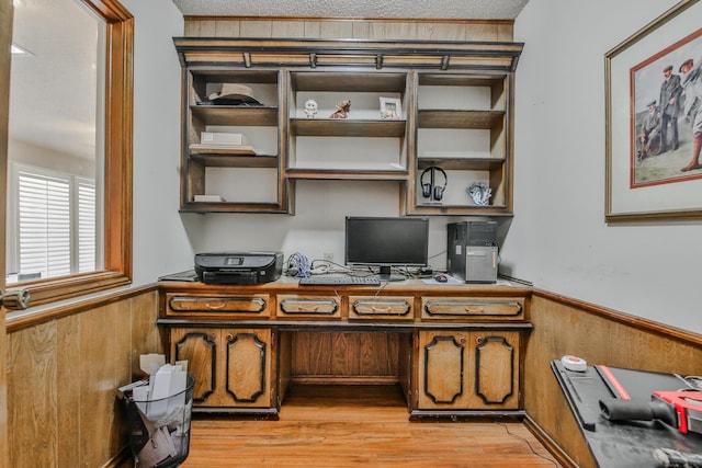 office space with wooden walls, built in desk, a textured ceiling, and light hardwood / wood-style flooring