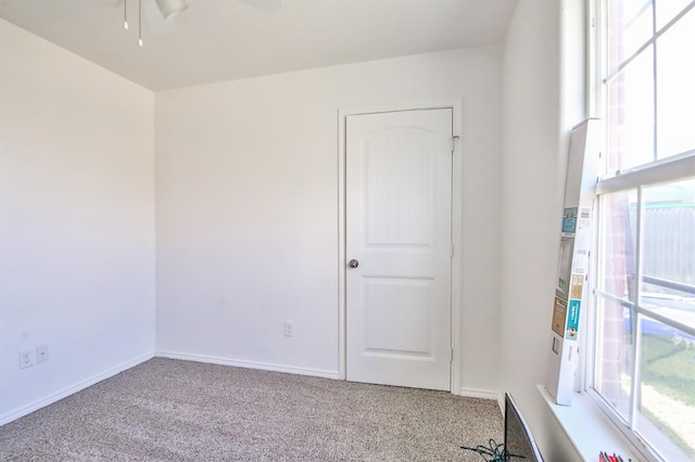 carpeted spare room featuring baseboards, a ceiling fan, and a wealth of natural light