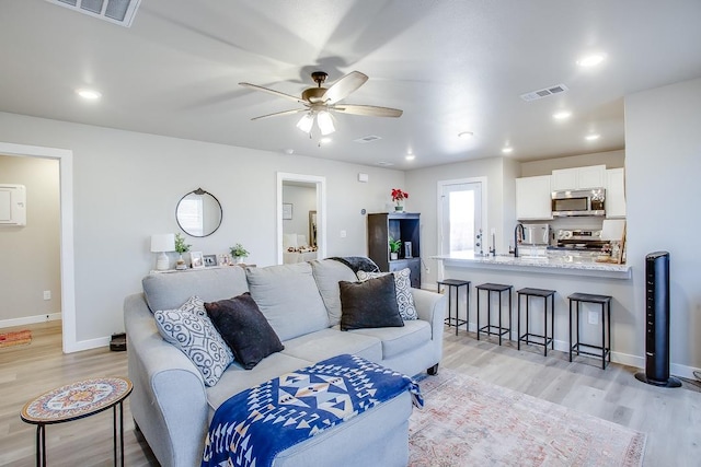 living room with sink, light hardwood / wood-style floors, and ceiling fan