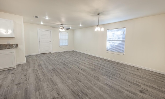 unfurnished living room with ceiling fan with notable chandelier and light hardwood / wood-style flooring