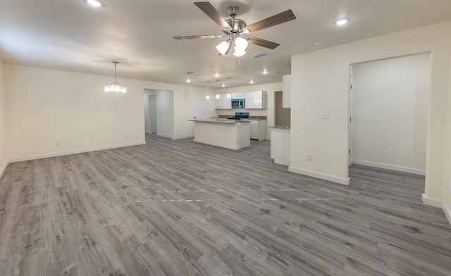 unfurnished living room with sink, ceiling fan with notable chandelier, and light hardwood / wood-style floors