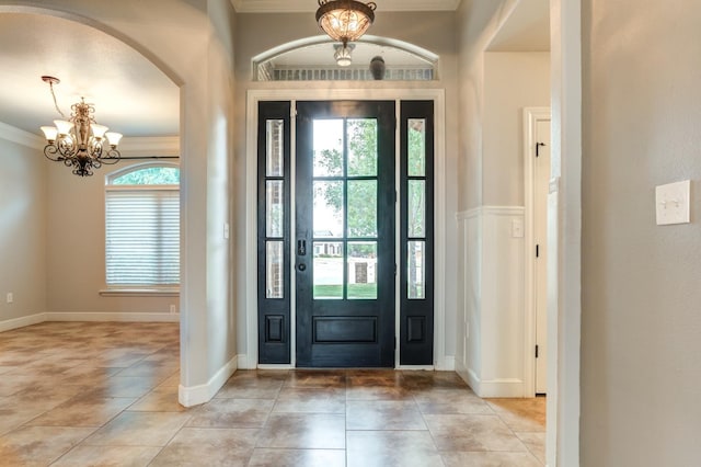 tiled foyer entrance featuring ornamental molding and a chandelier